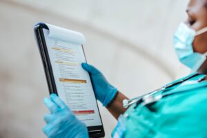 Medical professional in scrubs and mask reviewing compliance checklist with highlighted sections near Kenyan health facility